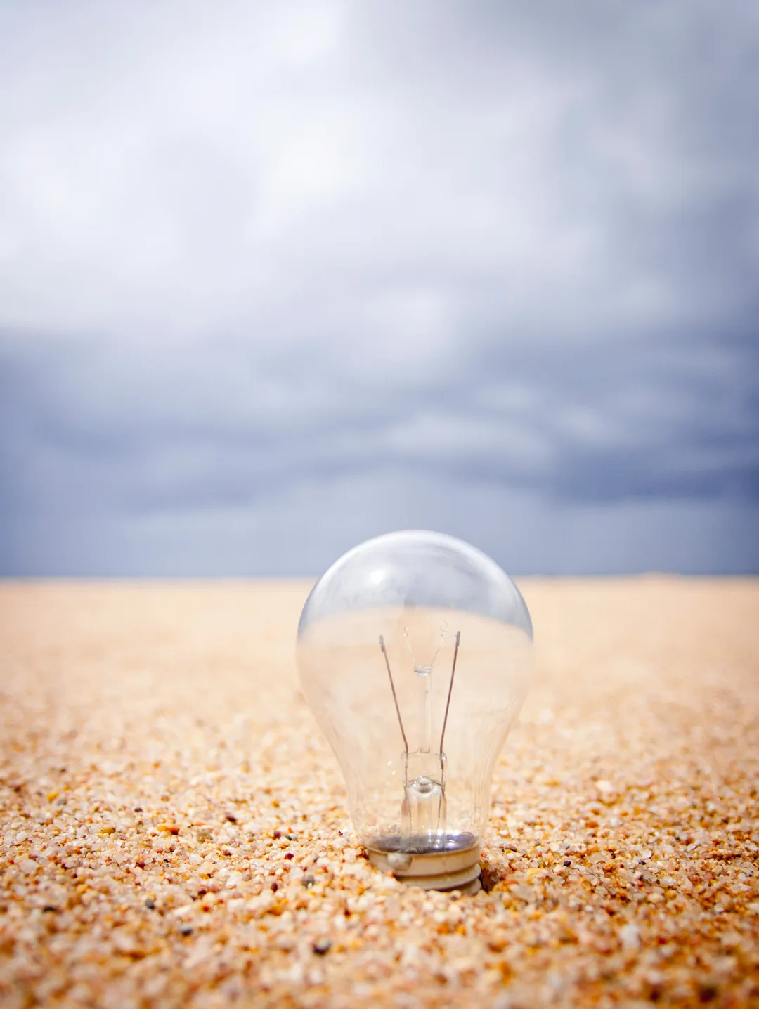 A glowing light bulb resting on sand at the shoreline